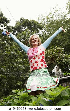 Stock Image - Low angle view of a mature woman smiling with her arms outstretched. Fotosearch