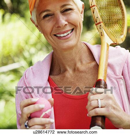 Stock Image - Portrait of a mature woman holding a tennis racket and a tennis ball. Fotosearch