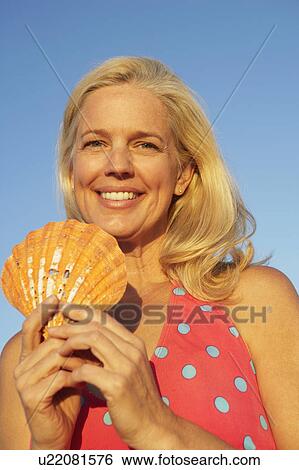 Stock Photograph - Portrait of a mature woman holding a seashell and smiling. Fotosearch