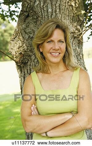Portrait of a mature woman leaning against a tree and smiling View Large Photo Image Stock Image - Portrait of a mature woman leaning against a tree and smiling. Fotosearch