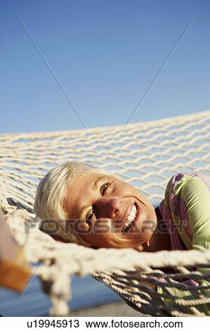 Stock Image - Portrait of a mature woman lying in a hammock and smiling. Fotosearch