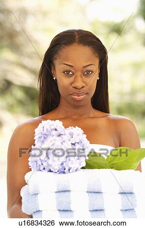 Stock Photograph - Portrait of a mid adult woman holding folded towels and a flower. Fotosearch