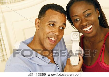 Stock Photo - Close-up of a mature man and a mid adult woman listening to a telephone receiver and smiling. Fotosearch
