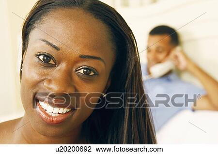 Stock Image - Portrait of a mid adult woman smiling with a man in the background. Fotosearch
