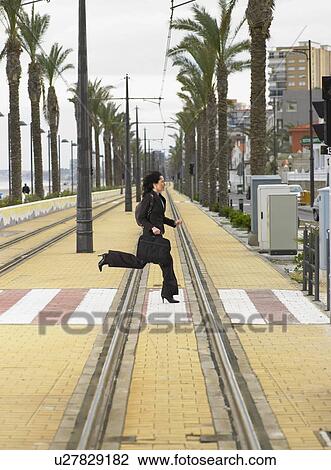 Stock Image - Businesswoman running across pedestrian crossing on tramway. Fotosearch