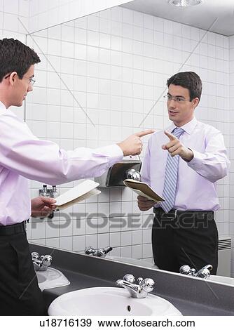 Stock Photo - Man practicing speech in office washroom mirror. Fotosearch