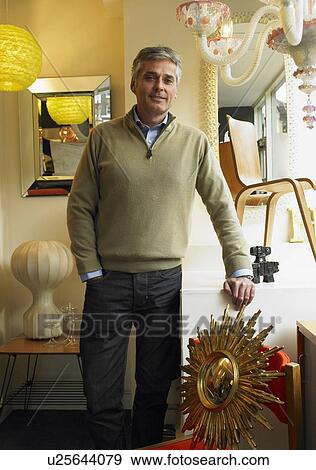 Stock Photo - Mature man standing in furniture shop, smiling, portrait. Fotosearch