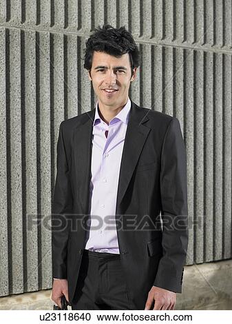 Stock Image - Portrait of young businessman near textured concrete wall, Alicante, Spain,. Fotosearch