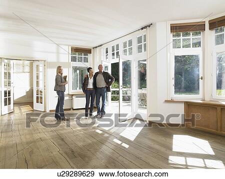 Stock Photo - Real estate agent showing empty house to a couple. Wide angle.. Fotosearch