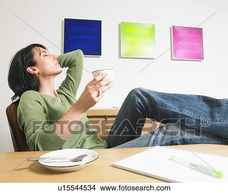 Picture - Relaxed businesswoman having a coffee and feet on desk.. Fotosearch