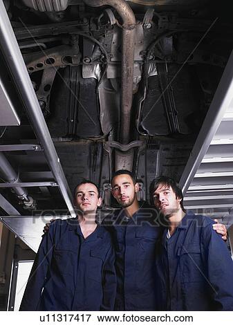 Three mechanics standing under a raised car View Large Photo Image Stock Photo - Three mechanics standing under a raised car. Fotosearch