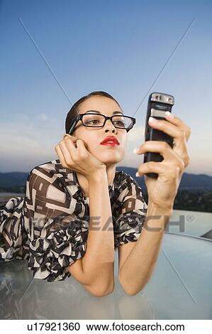 Stock Image - Woman leaning on table looking at cellular phone outdoors.. Fotosearch