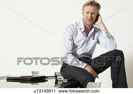 Stock Image - Young businessman seated on desk.. Fotosearch
