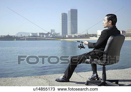 Stock Image - Business man fishing by seafront. Fotosearch