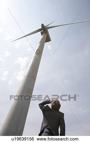 Stock Photograph - Businessman looking up at wind turbine. Fotosearch