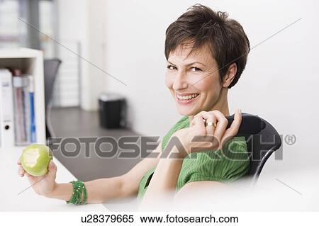 Woman eating an apple in her office View Large Photo Image Stock Photography - Woman eating an apple in her office. Fotosearch
