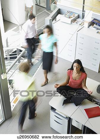 Stock Image - Young woman in a yoga position sitting on her work desk. Fotosearch