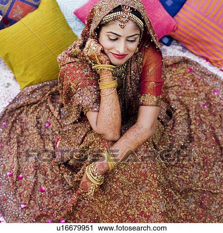 Stock Image - High angle view of a bride in a traditional wedding dress lying on the bed. Fotosearch