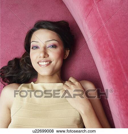 Stock Photo - High angle view of a young woman lying on couch and smiling. Fotosearch