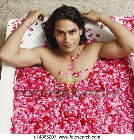 Stock Photo - Portrait of a young man lying in a bathtub filled with rose petals. Fotosearch