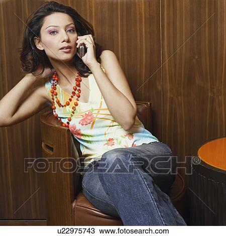 Portrait of a young woman sitting on a chair and talking on a mobile phone View Large Photo Image Stock Image - Portrait of a young woman sitting on a chair and talking on a mobile phone. Fotosearch