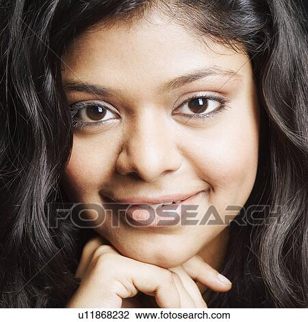 Stock Image - Portrait of a young woman smiling with her hand on her chin. Fotosearch