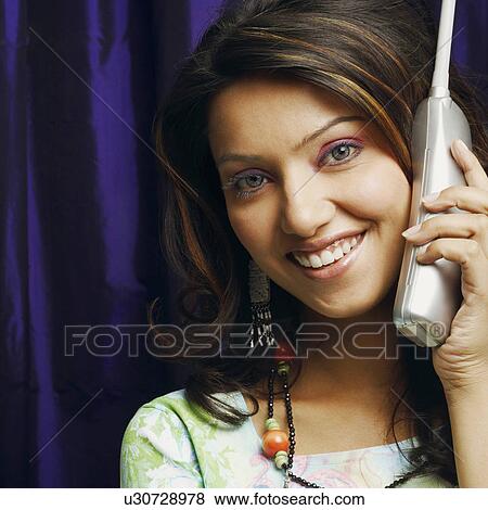 Portrait of a young woman talking on a cordless phone and smiling View Large Photo Image Stock Photo - Portrait of a young woman talking on a cordless phone and smiling. Fotosearch