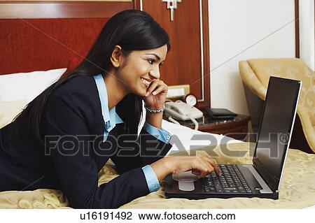 Businesswoman lying on the bed and using a laptop View Large Photo Image Stock Image - Businesswoman lying on the bed and using a laptop. Fotosearch