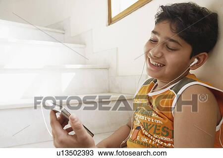 Stock Image - Close-up of a boy sitting on steps and listening to an MP3 player. Fotosearch