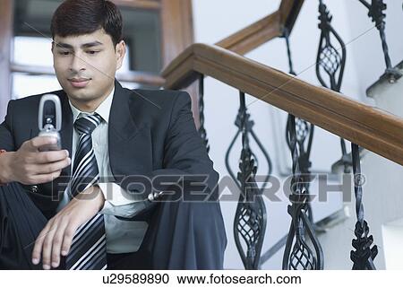 Stock Image - Close-up of a businessman sitting on a staircase and operating a mobile phone. Fotosearch