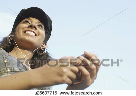 Stock Photography - Low angle view of a young woman wearing earphones listening to music. Fotosearch