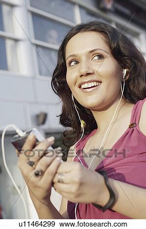 Stock Photo - Low angle view of young woman listening to an MP3 player. Fotosearch