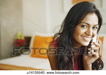 Portrait of a young woman talking on a cordless phone and smiling View Large Photo Image Stock Image - Portrait of a young woman talking on a cordless phone and smiling. Fotosearch