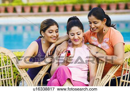 Three young women looking at a mobile phone and smiling View Large Photo Image Stock Photo - Three young women looking at a mobile phone and smiling. Fotosearch