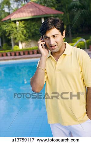 Stock Photo - Young man talking on a mobile phone at the poolside. Fotosearch