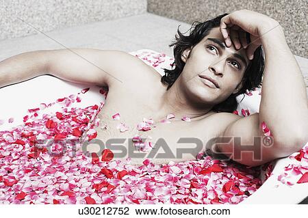Stock Image - Close-up of a young man lying in a bathtub filled with rose petals. Fotosearch
