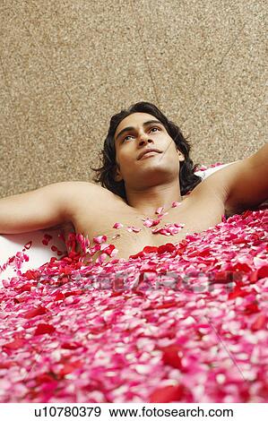 Stock Photo - Close-up of a young man lying in a bathtub filled with rose petals. Fotosearch