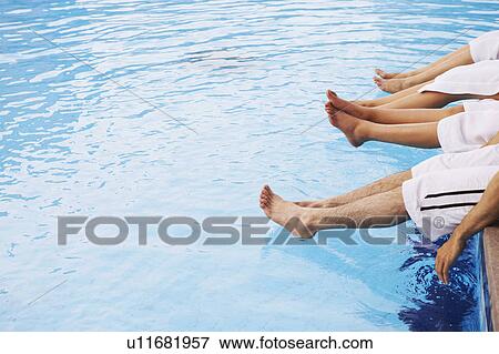 Stock Photo - Low section view of four people sitting together near a swimming pool. Fotosearch