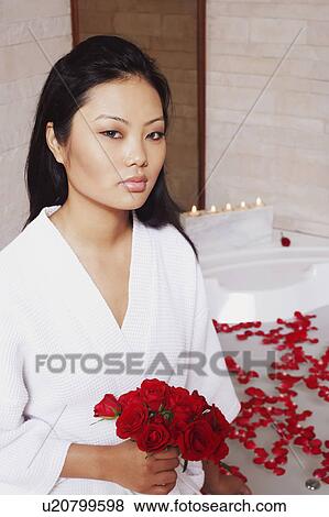 Stock Photo - Portrait of a young woman holding a bunch of roses near a bathtub. Fotosearch