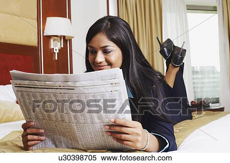 Stock Photography - Close-up of a businesswoman lying on the bed and reading a newspaper. Fotosearch
