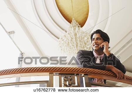 Low angle view of a businessman leaning over a railing and talking on a mobile phone View Large Photo Image Stock Photo - Low angle view of a businessman leaning over a railing and talking on a mobile phone. Fotosearch