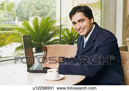 Stock Image - Portrait of a businessman using a laptop in a cafeteria. Fotosearch