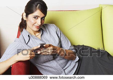 Stock Photo - Portrait of a young woman lying on a couch and holding a mobile phone. Fotosearch