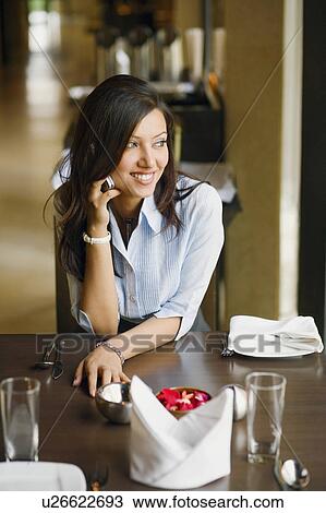 Stock Image - Young woman talking on a mobile phone in a restaurant. Fotosearch