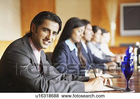 Stock Photo - Portrait of a businessman sitting with his colleagues in a conference room and smiling. Fotosearch