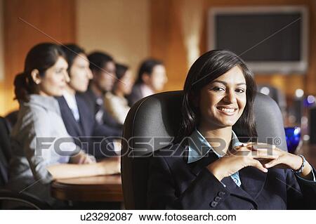 Stock Photo - Portrait of a businesswoman sitting with her colleagues in a conference room and smiling. Fotosearch