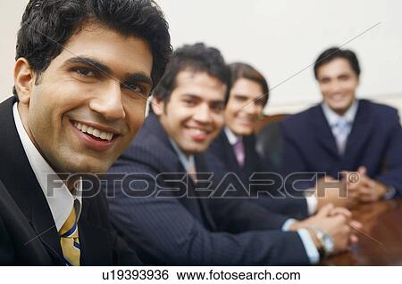 Stock Photograph - Portrait of four businessmen sitting in a conference room. Fotosearch