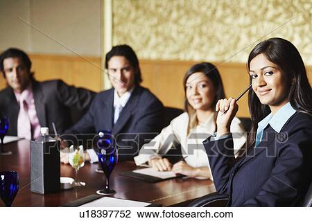 Stock Image - Portrait of two businesswomen and two businessmen sitting in a conference room and smiling. Fotosearch