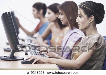 Stock Image - Side profile of four businesswomen in front of computers. Fotosearch