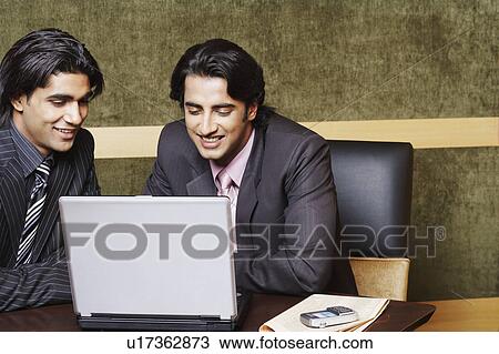 Two businessmen sitting in an office and using a laptop View Large Photo Image Stock Image - Two businessmen sitting in an office and using a laptop. Fotosearch